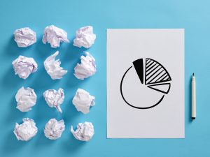 A sheet of paper with a pie chart is placed on a blue surface, surrounded by crumpled paper balls. A marker is next to the paper.